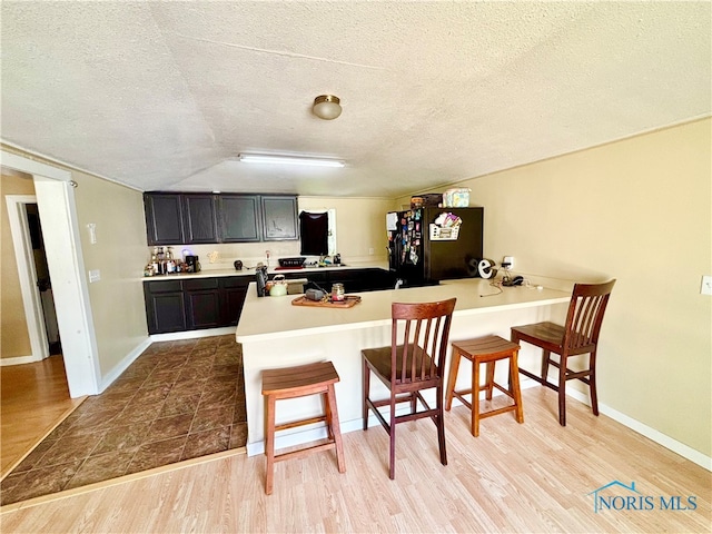 307 Spencerville St, Hicksville, OH 43526 - kitchen featuring freestanding refrigerator, a breakfast bar area, a peninsula, a textured ceiling, and dark cabinets