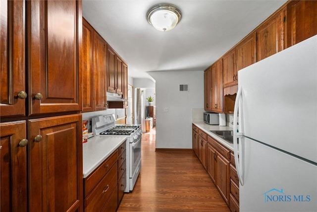 2958 Penrose Ave, Toledo, OH 43614 - kitchen featuring white appliances, light countertops, dark wood-type flooring, under cabinet range hood, and brown cabinets