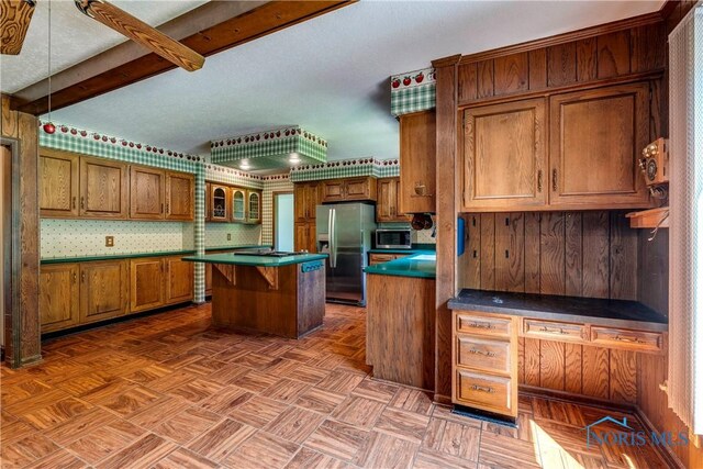 6608 Inglewood Dr, Holland, OH 43528 - kitchen featuring appliances with stainless steel finishes, brown cabinetry, a center island, dark countertops, and beamed ceiling