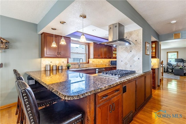 312 W Dudley St, Maumee, OH 43537 - kitchen featuring island exhaust hood, a textured ceiling, stainless steel appliances, light wood-type flooring, and a breakfast bar area