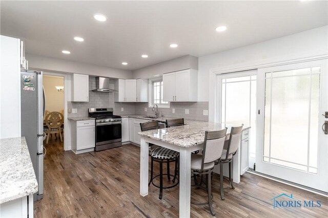 6842 Shieldwood Rd, Toledo, OH 43617 - kitchen with stainless steel appliances, wall chimney range hood, decorative backsplash, dark wood finished floors, and white cabinetry