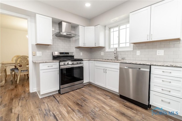 6842 Shieldwood Rd, Toledo, OH 43617 - kitchen featuring stainless steel appliances, wall chimney range hood, white cabinets, wood finished floors, and decorative backsplash
