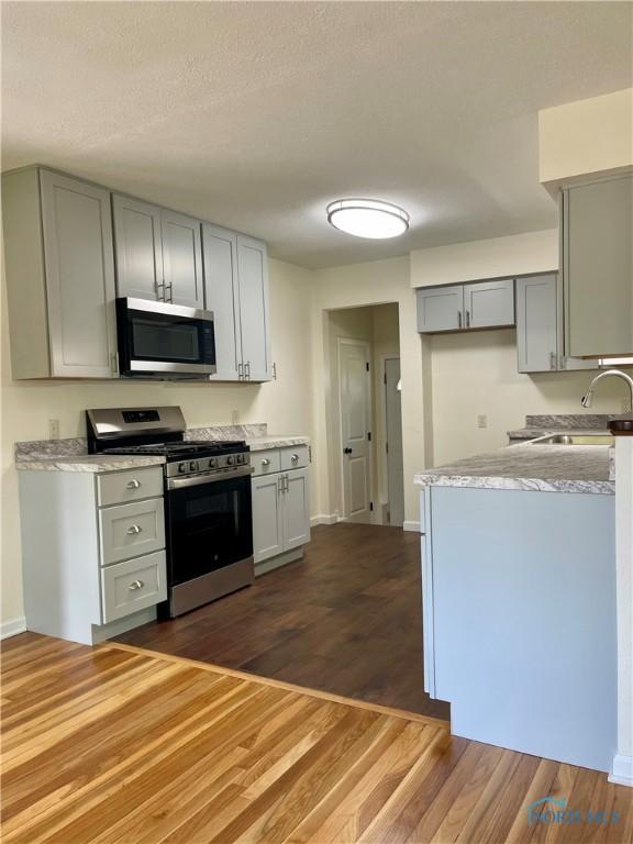 4846 Amesbury Rd, Toledo, OH 43612 - kitchen with appliances with stainless steel finishes, gray cabinets, dark wood-style floors, a textured ceiling, and light stone counters