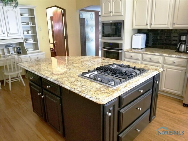 3704 Brookside Rd, Ottawa Hills, OH 43606 - kitchen with appliances with stainless steel finishes, white cabinets, arched walkways, and light wood-style flooring