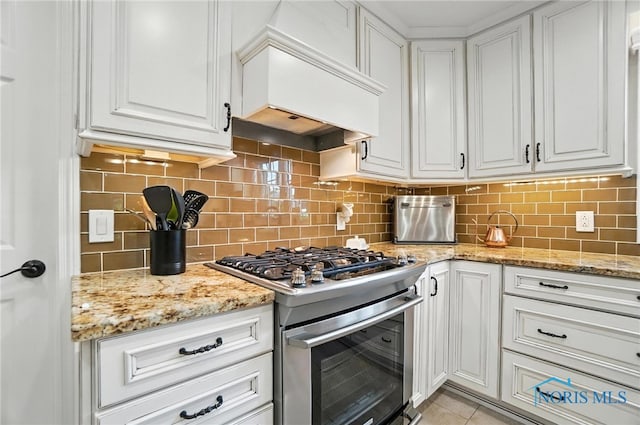 5576 N Citation Rd, Ottawa Hills, OH 43615 - kitchen featuring stainless steel gas range oven, white cabinets, backsplash, premium range hood, and light tile patterned floors
