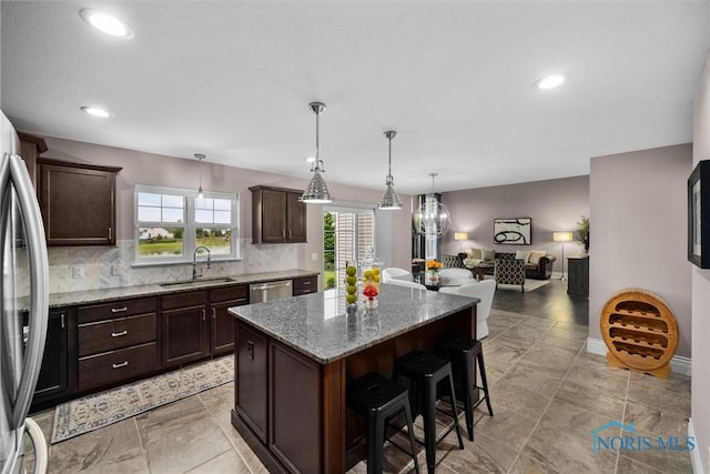 9258 Nate Ct, Sylvania, OH 43560 - kitchen with appliances with stainless steel finishes, a center island, a kitchen bar, dark brown cabinets, and light stone counters