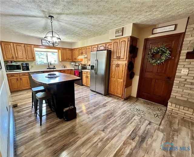 210 Duck Pond Rd, Upper Sandusky, OH 43351 - kitchen with appliances with stainless steel finishes, light wood finished floors, brown cabinetry, a chandelier, and a textured ceiling