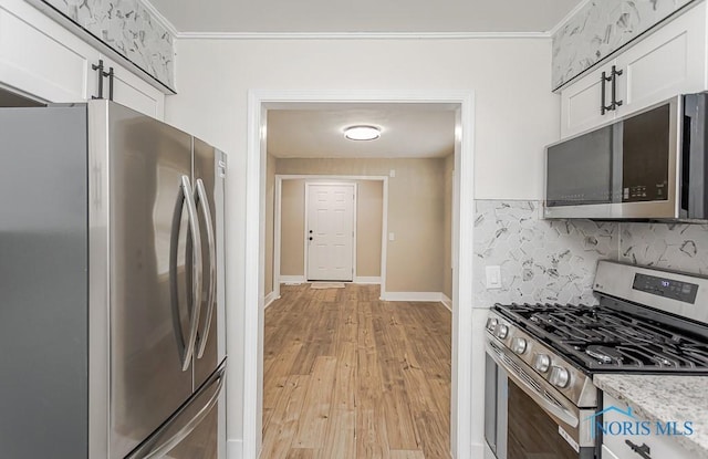 4308 Willis Blvd, Toledo, OH 43623 - kitchen with appliances with stainless steel finishes, backsplash, white cabinets, light wood finished floors, and ornamental molding