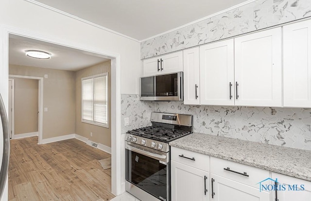4308 Willis Blvd, Toledo, OH 43623 - kitchen with stainless steel appliances, decorative backsplash, white cabinets, light wood finished floors, and crown molding