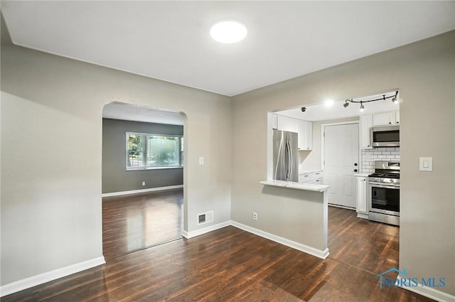 2838 Secor Rd, Toledo, OH 43606 - kitchen featuring appliances with stainless steel finishes, white cabinetry, dark wood-style flooring, arched walkways, and tasteful backsplash