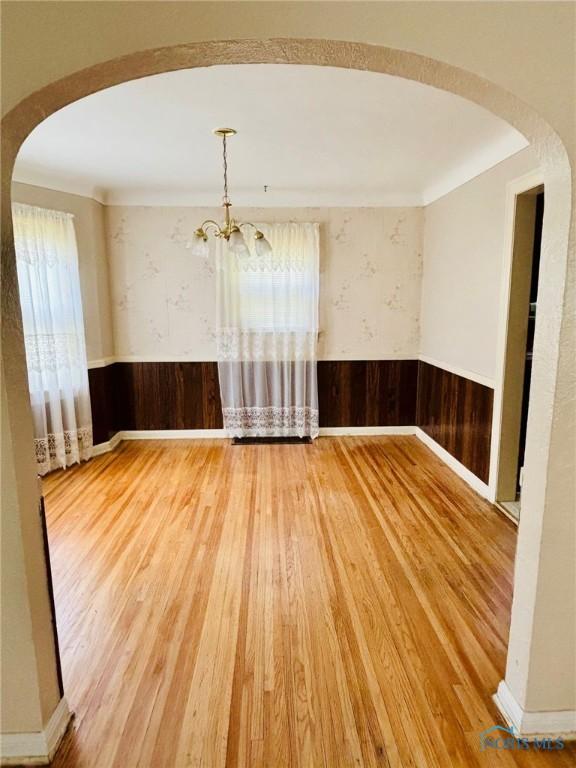 4136 Berwick Ave, Toledo, OH 43612 - empty room featuring arched walkways, wood finished floors, wainscoting, a chandelier, and wood walls