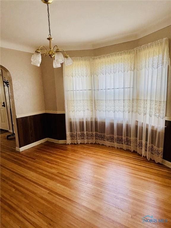 4136 Berwick Ave, Toledo, OH 43612 - empty room featuring arched walkways, a chandelier, wood finished floors, and wainscoting