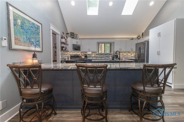 8411 Larch Rd, Toledo, OH 43617 - kitchen featuring vaulted ceiling, stainless steel appliances, a peninsula, a kitchen bar, and backsplash