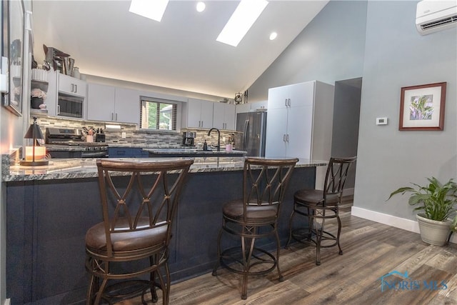 8411 Larch Rd, Toledo, OH 43617 - kitchen with stainless steel appliances, a wall unit AC, a kitchen breakfast bar, backsplash, and dark wood finished floors