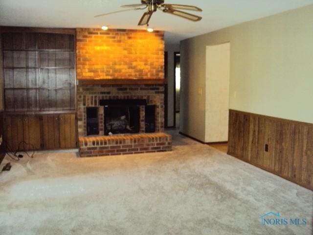 217 Lakeview Dr, Bryan, OH 43506 - unfurnished living room featuring ceiling fan, carpet, wood walls, a wainscoted wall, and a brick fireplace
