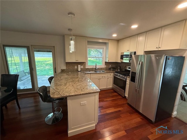 9151 Rolling Hill Rd, Holland, OH 43528 - kitchen with stainless steel appliances, a peninsula, white cabinets, dark wood finished floors, and hanging light fixtures
