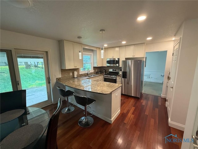 9151 Rolling Hill Rd, Holland, OH 43528 - kitchen featuring appliances with stainless steel finishes, a peninsula, white cabinets, dark wood finished floors, and decorative light fixtures