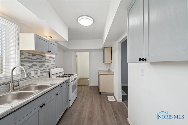 1155 Pinewood Ave, Toledo, OH 43607 - kitchen featuring white range with gas stovetop, wood finished floors, backsplash, gray cabinetry, and light countertops