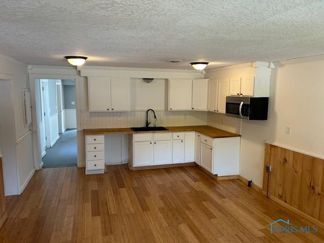 203 S Main, Hicksville, OH 43526 - kitchen featuring wood finished floors, white cabinets, stainless steel microwave, a textured ceiling, and decorative backsplash