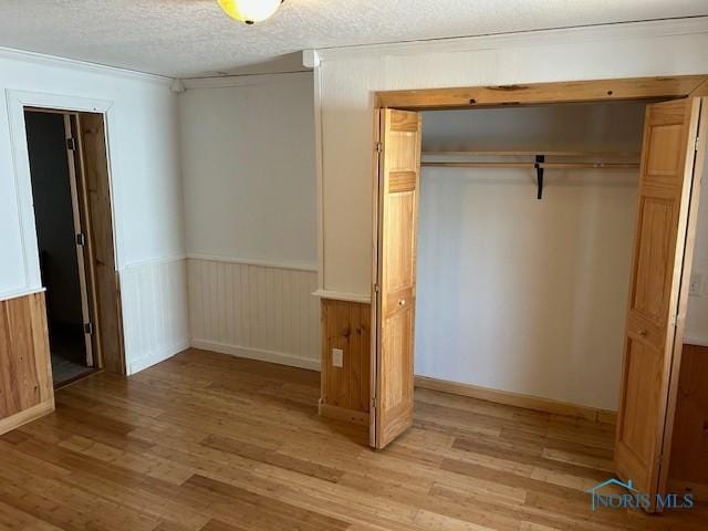 203 S Main, Hicksville, OH 43526 - unfurnished bedroom featuring a closet, light wood-type flooring, wainscoting, and a textured ceiling