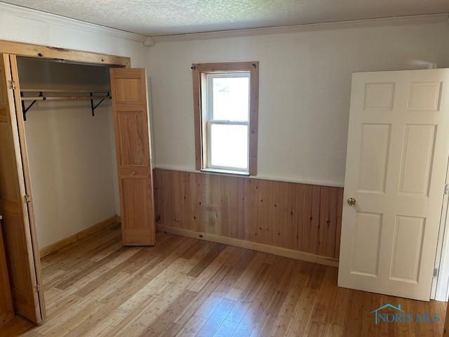 203 S Main, Hicksville, OH 43526 - unfurnished bedroom featuring wainscoting, light wood-style flooring, ornamental molding, a closet, and wood walls