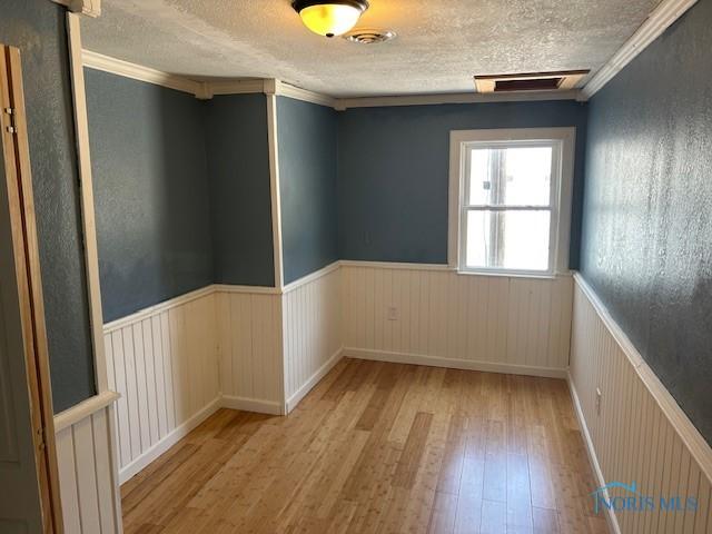 203 S Main, Hicksville, OH 43526 - unfurnished room featuring wood-type flooring, a wainscoted wall, a textured ceiling, and crown molding