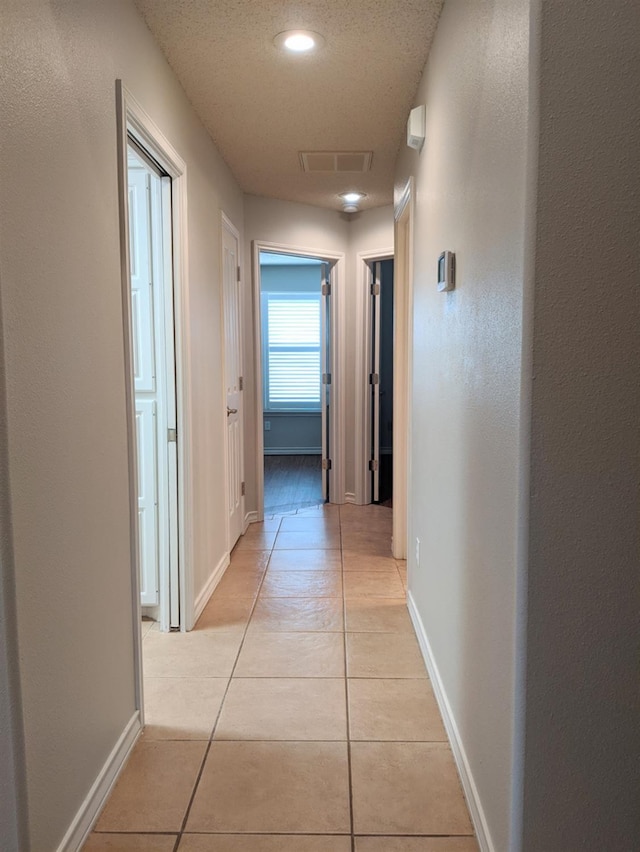 hallway with a textured ceiling and light tile patterned flooring