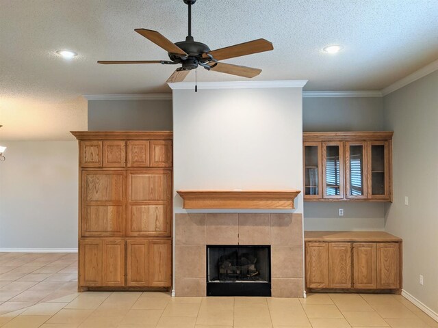 unfurnished living room featuring a tile fireplace, light tile patterned flooring, ornamental molding, ceiling fan, and a textured ceiling