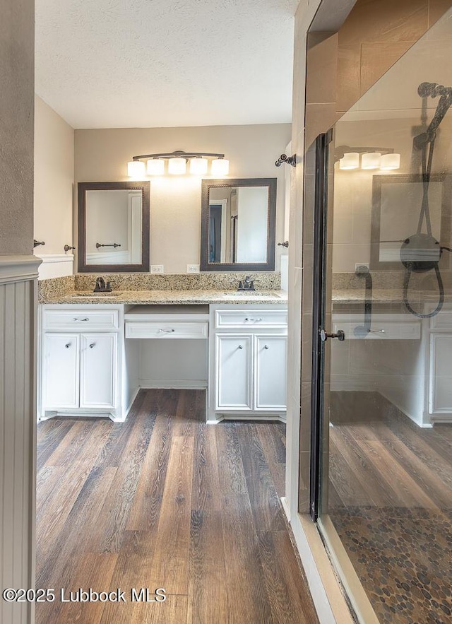3423 60th St, Lubbock, TX 79413 - bathroom with a shower stall, wood finished floors, double vanity, and a textured ceiling