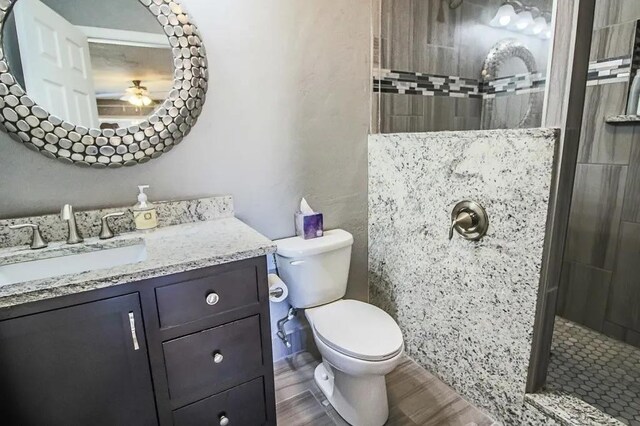 bathroom with hardwood / wood-style flooring, vanity, toilet, and a tile shower