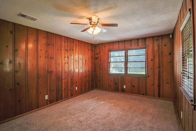 carpeted spare room with a textured ceiling, ceiling fan, and wood walls