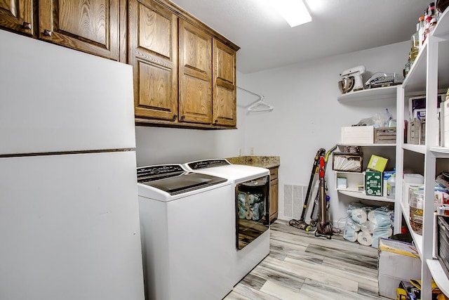 laundry room featuring cabinets, washer and clothes dryer, and light hardwood / wood-style flooring