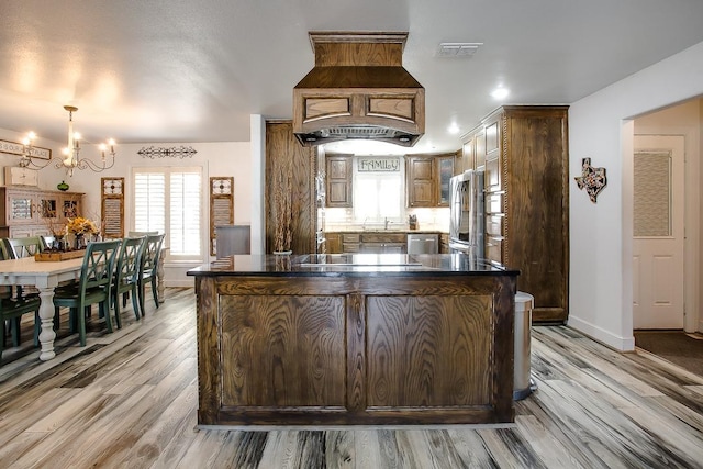 kitchen with a notable chandelier, light hardwood / wood-style flooring, stainless steel appliances, and custom range hood