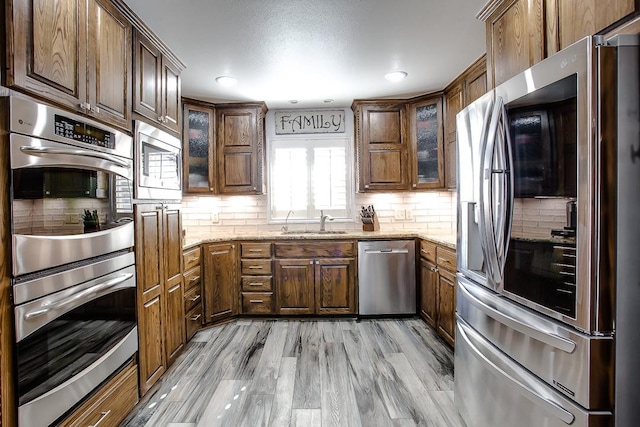 kitchen with sink, light stone counters, appliances with stainless steel finishes, light hardwood / wood-style floors, and backsplash