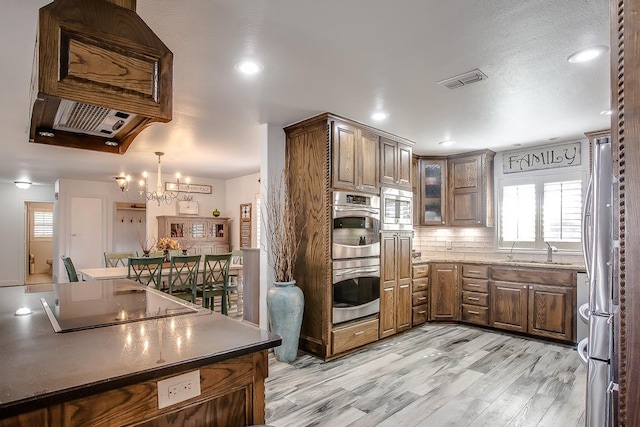 kitchen with sink, backsplash, stainless steel appliances, a notable chandelier, and light hardwood / wood-style floors