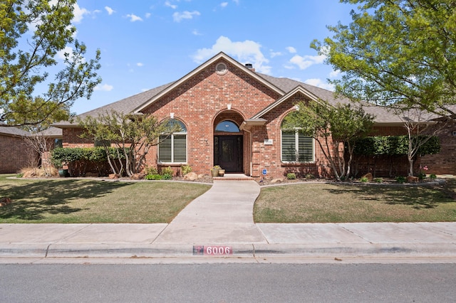 ranch-style house featuring brick siding, a shingled roof, and a front yard