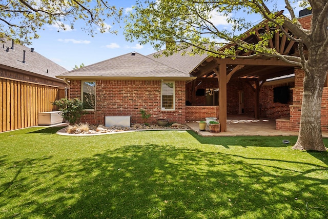 back of house with brick siding, roof with shingles, a yard, and a patio area