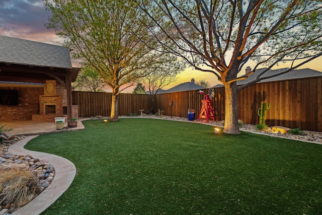 yard at dusk with a patio, a fireplace, and a fenced backyard