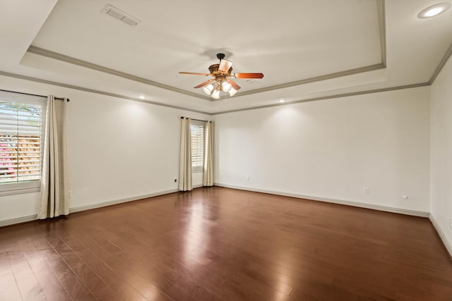 spare room with a ceiling fan, visible vents, dark wood-style flooring, and a tray ceiling