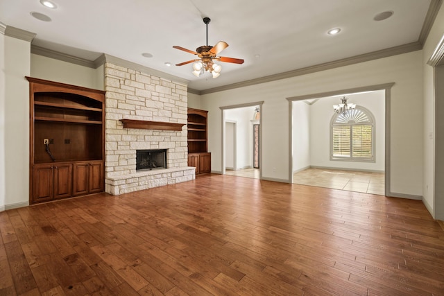 unfurnished living room featuring a fireplace, wood-type flooring, crown molding, baseboards, and ceiling fan with notable chandelier