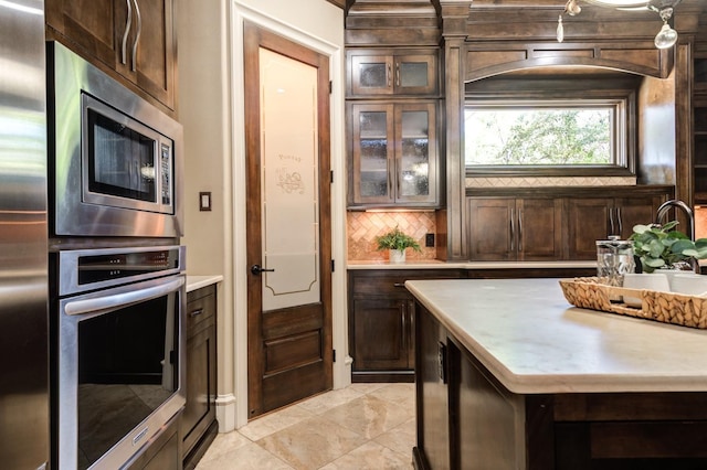 kitchen with appliances with stainless steel finishes, light tile patterned floors, dark brown cabinets, and backsplash