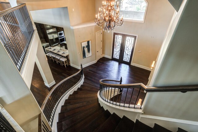 entryway with a towering ceiling, dark wood-type flooring, french doors, and a chandelier