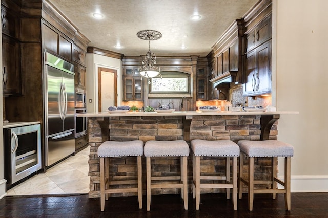 bar featuring dark brown cabinets, built in appliances, wine cooler, and backsplash