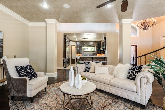 living room with crown molding, dark wood-type flooring, decorative columns, and ceiling fan with notable chandelier