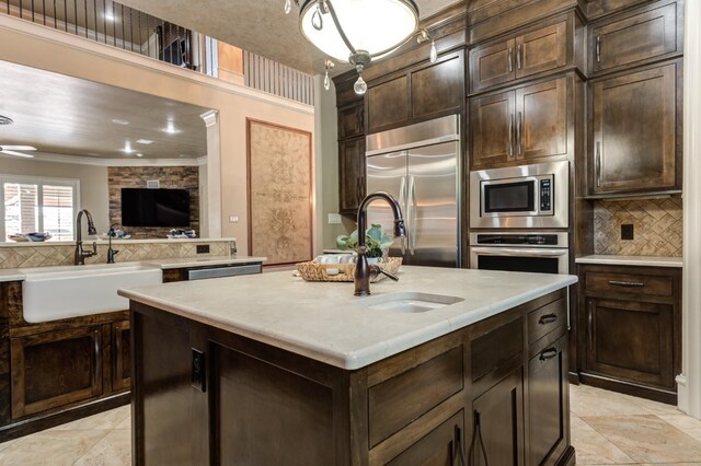 kitchen featuring built in appliances, sink, dark brown cabinetry, and a center island with sink