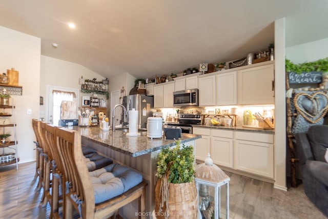 kitchen featuring vaulted ceiling, white cabinetry, appliances with stainless steel finishes, and a breakfast bar