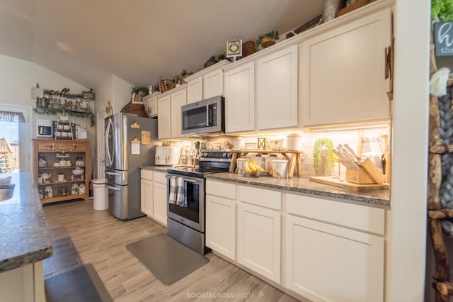 kitchen featuring light hardwood / wood-style flooring, stainless steel appliances, white cabinets, vaulted ceiling, and dark stone counters