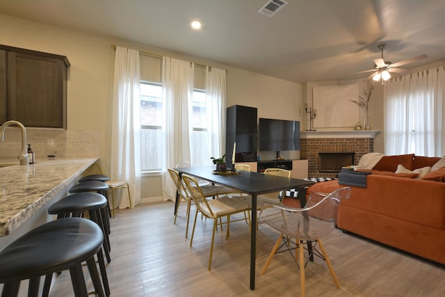 dining space featuring ceiling fan, sink, a fireplace, and light hardwood / wood-style flooring