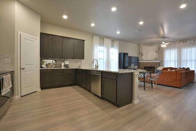 kitchen featuring sink, dark brown cabinets, light hardwood / wood-style flooring, dishwasher, and a fireplace