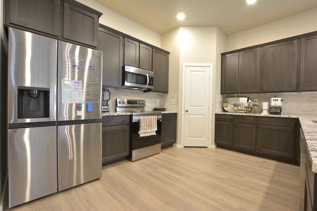 kitchen with appliances with stainless steel finishes, light stone countertops, and dark brown cabinets